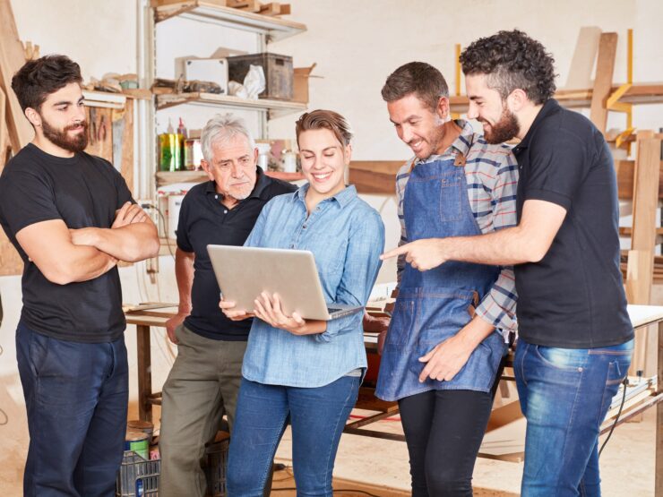 Team steht in einer Werkstatt und schaut auf einen Laptop
