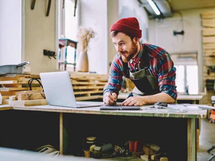 Mann in einer Werkstatt schaut auf einen Laptop und macht sich Notizen